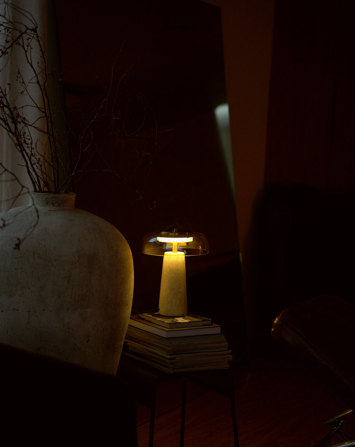 The Ankaa lamp lit on a stack of magazines in front of a leaning mirror.