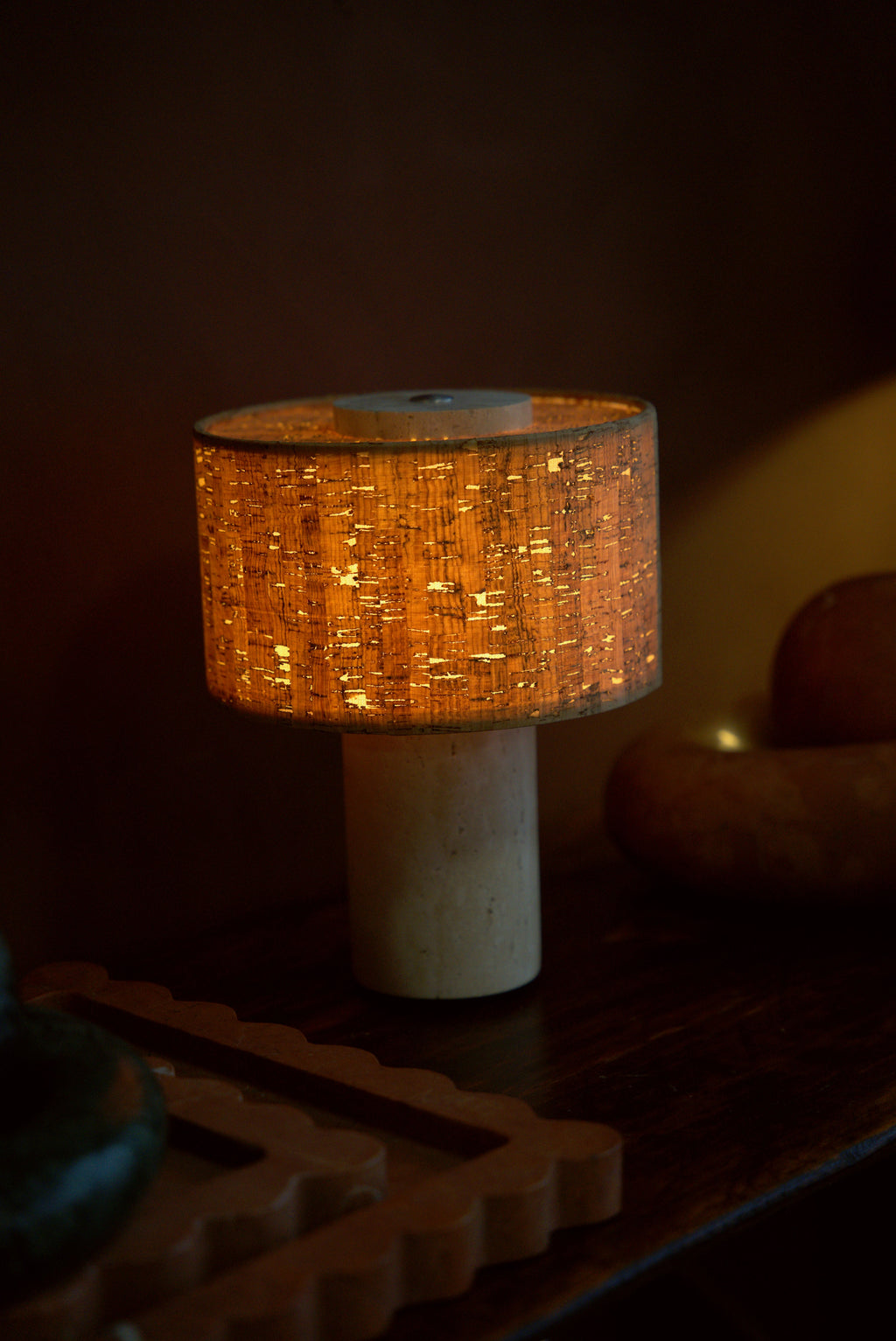 The Dorado lamp lit on a dark wood console among stone objects.