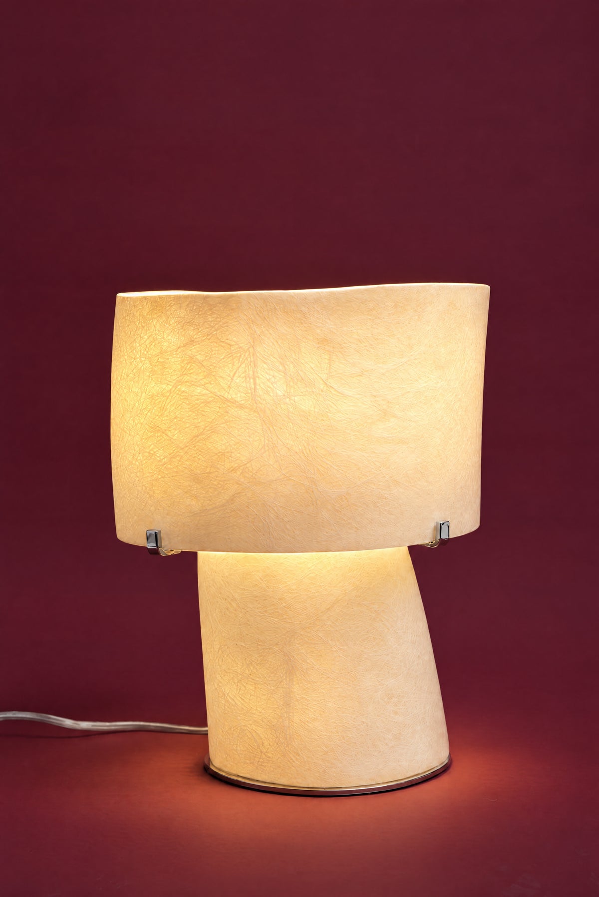 The Atria lamp, lit: the drum and foot glowing warm cream-gold like a lantern, the fibreglass strands lit through.