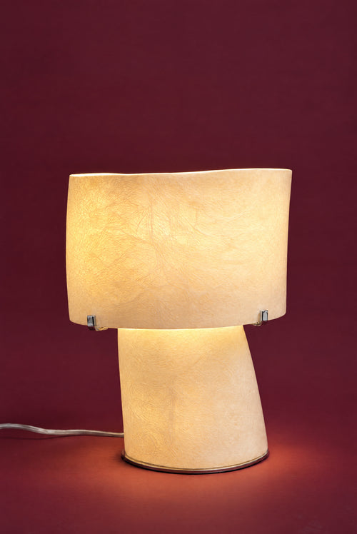 The Atria lamp, lit: the drum and foot glowing warm cream-gold like a lantern, the fibreglass strands lit through.