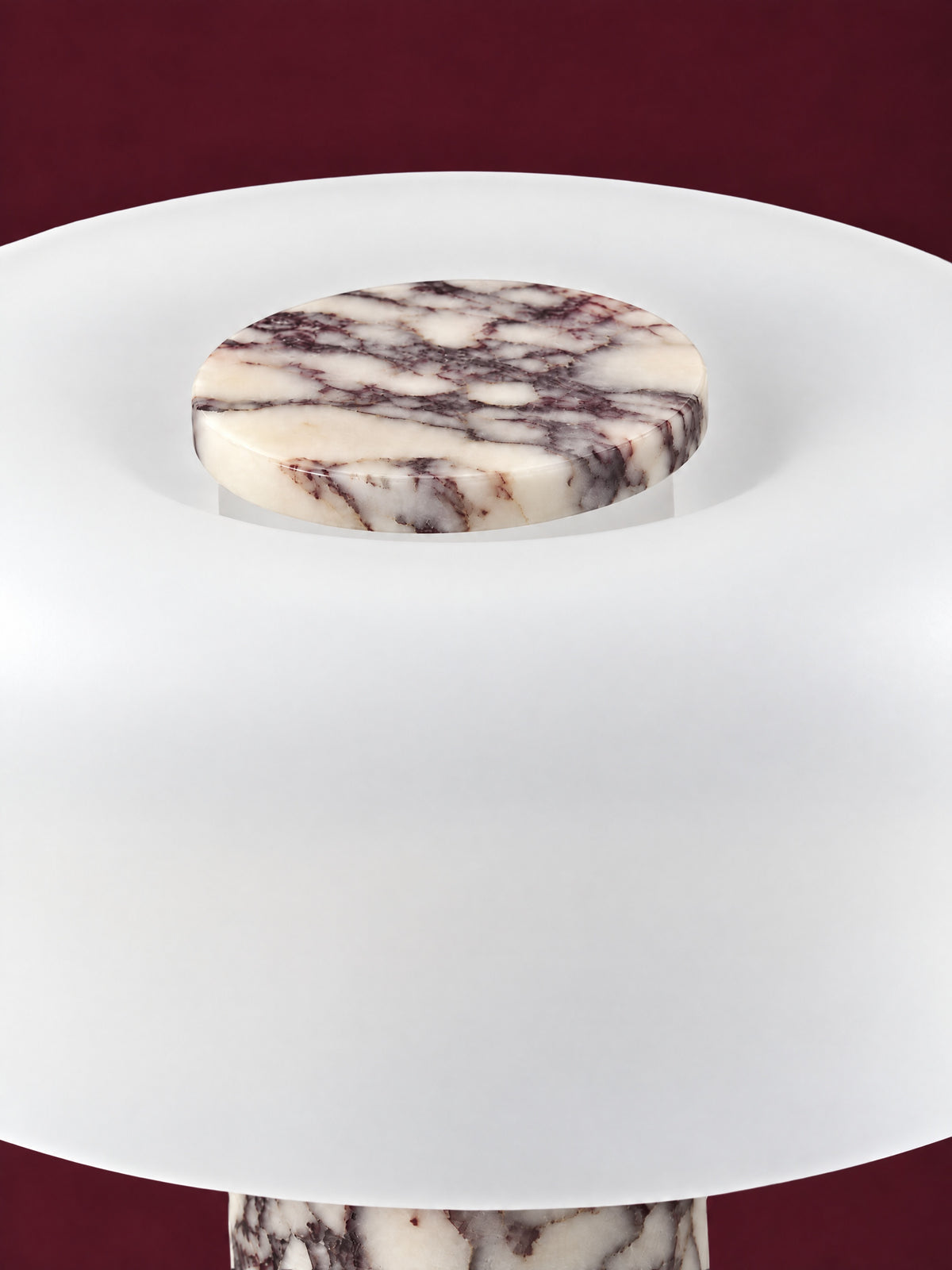 The Caelum lamp in Calacatta Viola from above: the marble disc set into the crown of the frosted glass dome, against a deep oxblood background.