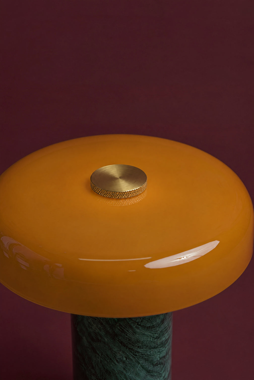Close-up of the knurled brass touch-dimmer cap in the centre of the Columba lamp's amber glass disc.