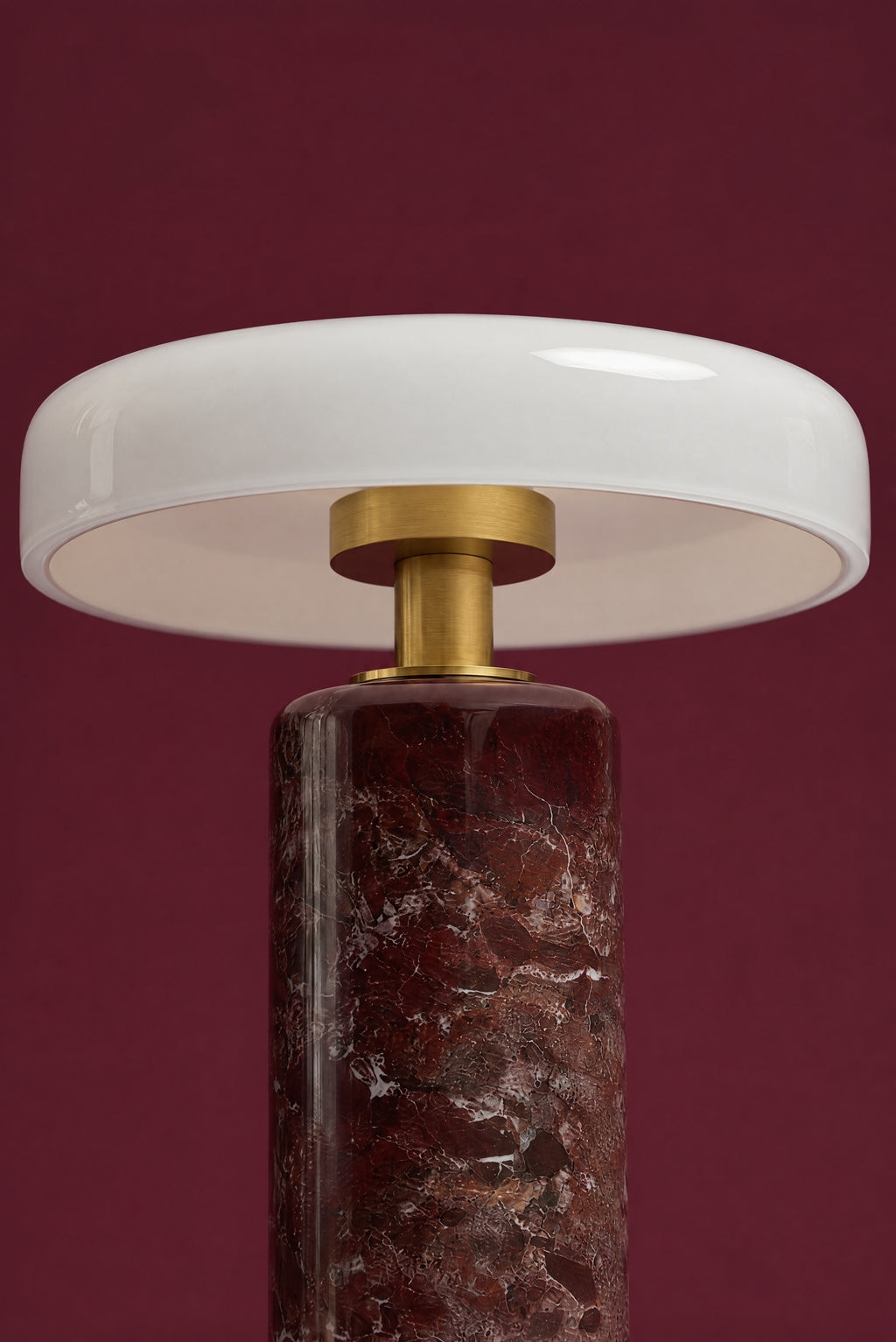 Under the disc of the Columba lamp, seen straight on: the white inside of the opal glass shade, the brass cup and stem, and the brass collar on the red marble column.