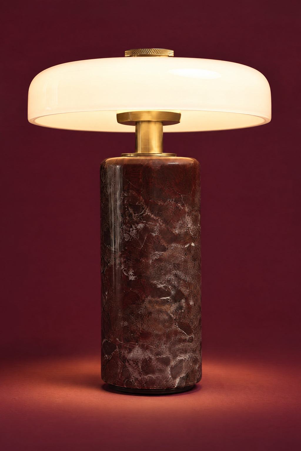 The Columba lamp lit: the white opal disc glowing warm and even, light pooling on the floor around the dark red marble column.