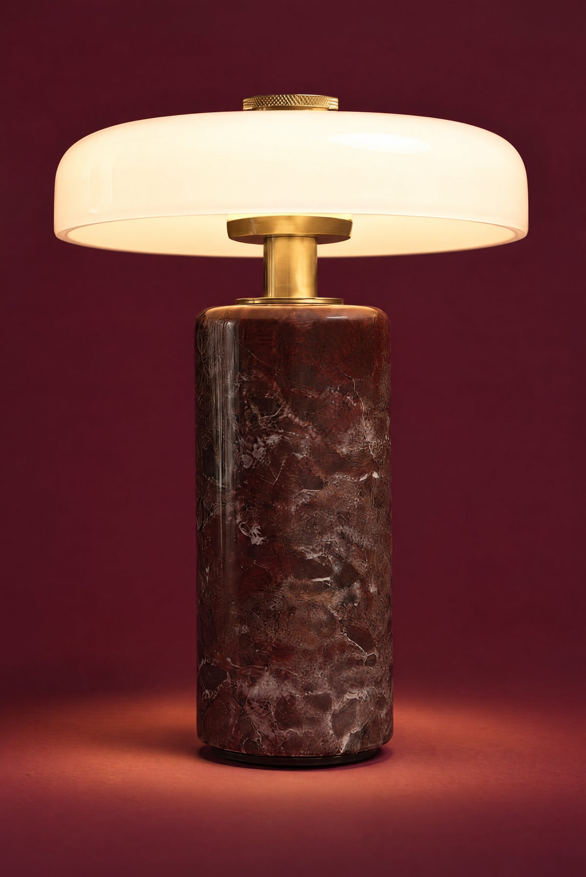 The Columba lamp lit: the white opal disc glowing warm and even, light pooling on the floor around the dark red marble column.