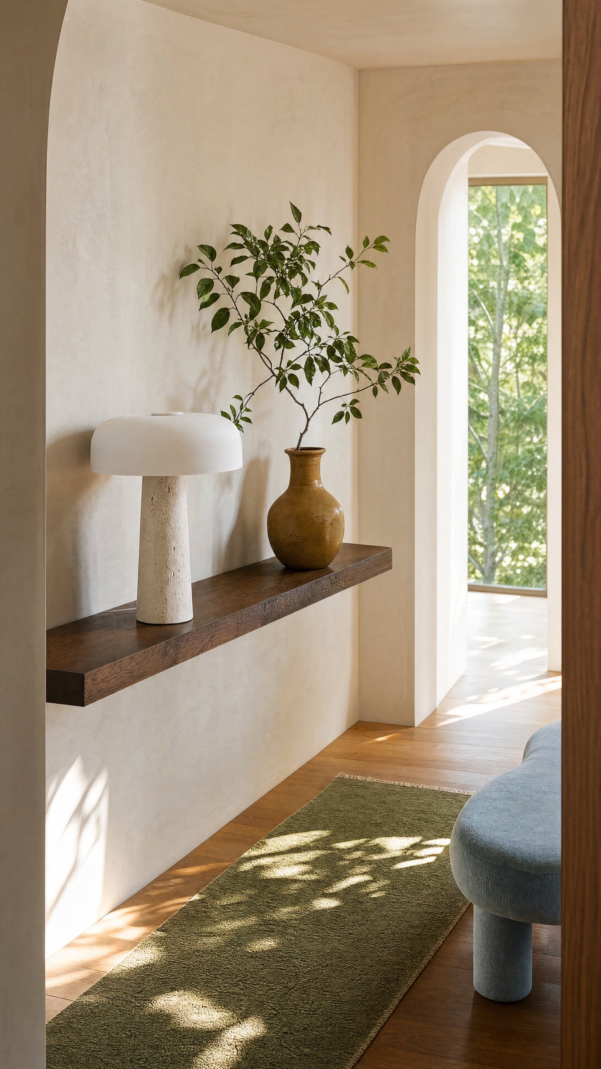 The Caelum lamp unlit on a floating walnut shelf in a hallway, a clay vase with a leafy branch beside it and a green runner below.