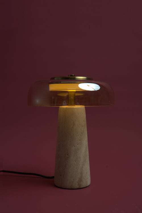 The Ankaa lamp, lit: the rose glass dome glowing amber-red over the warmly lit travertine cone.