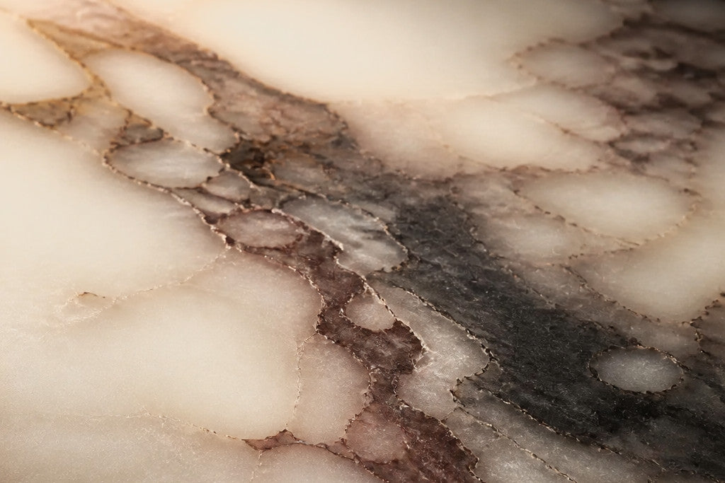 Calacatta Viola, close: plum and oxide veining over a cream ground, lit warm from one side so the stone goes translucent at the edge.