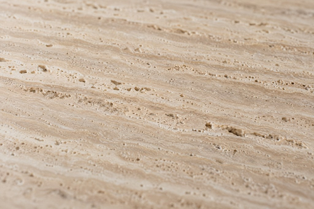 Travertine, close: warm sandy beige stone with fine layered banding and small open pores, honed.