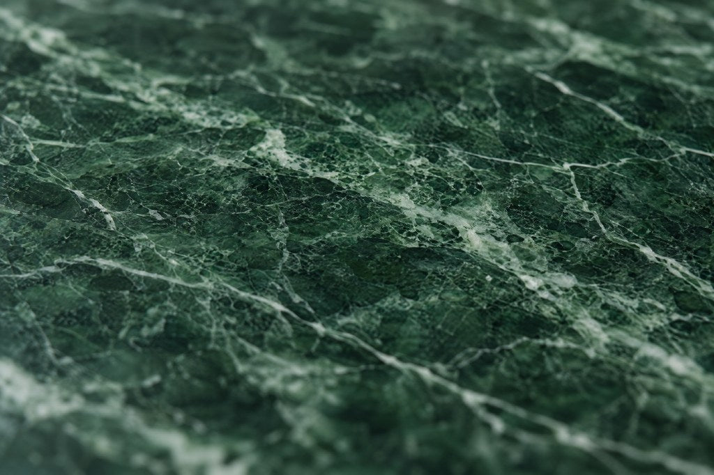 Verde marble, close: fine white and pale green veins over a deep forest-green ground, polished.